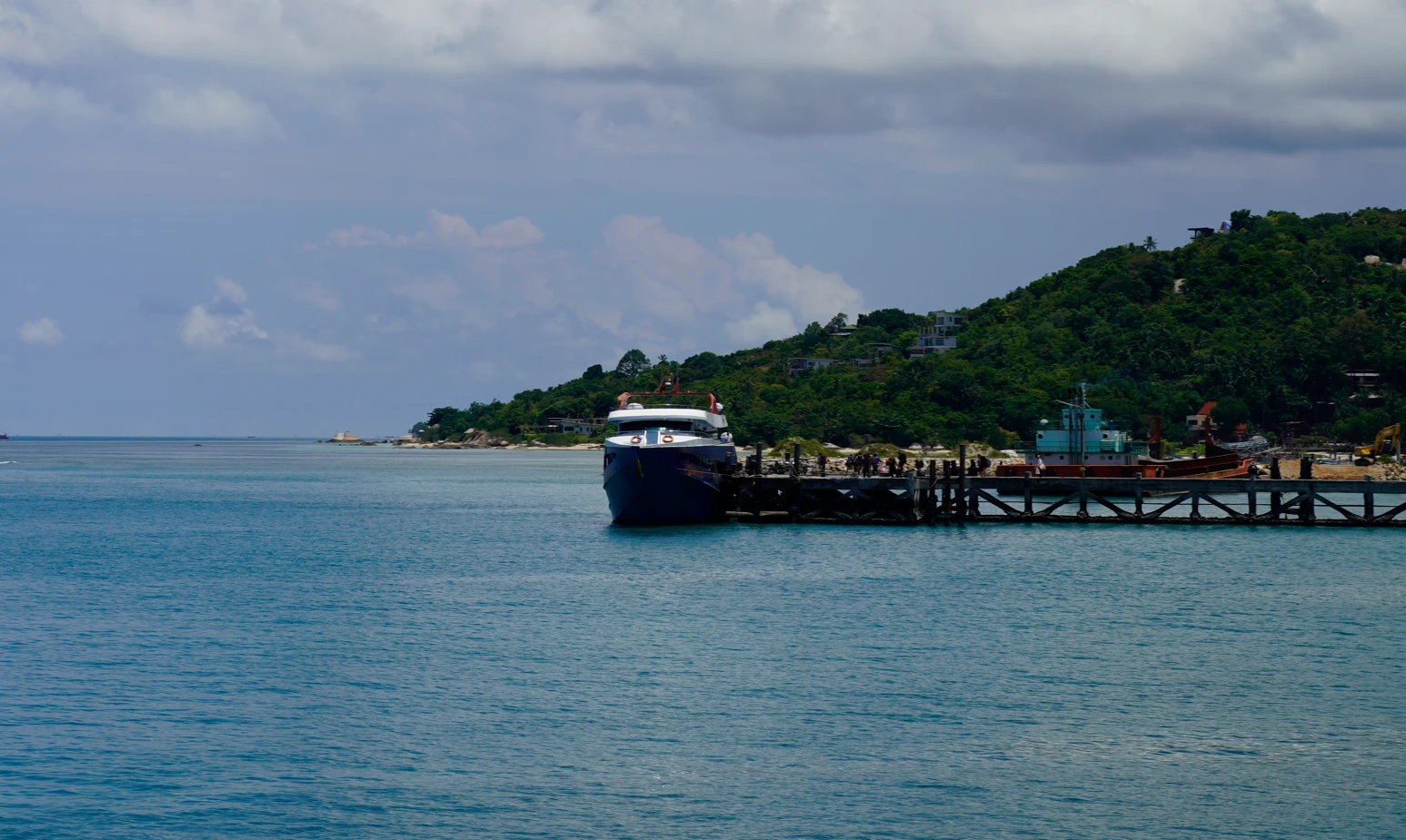 A Songserm ferry moored at the pier in Thong Sala on Koh Phangan, with a green hill and turquoise water behind it